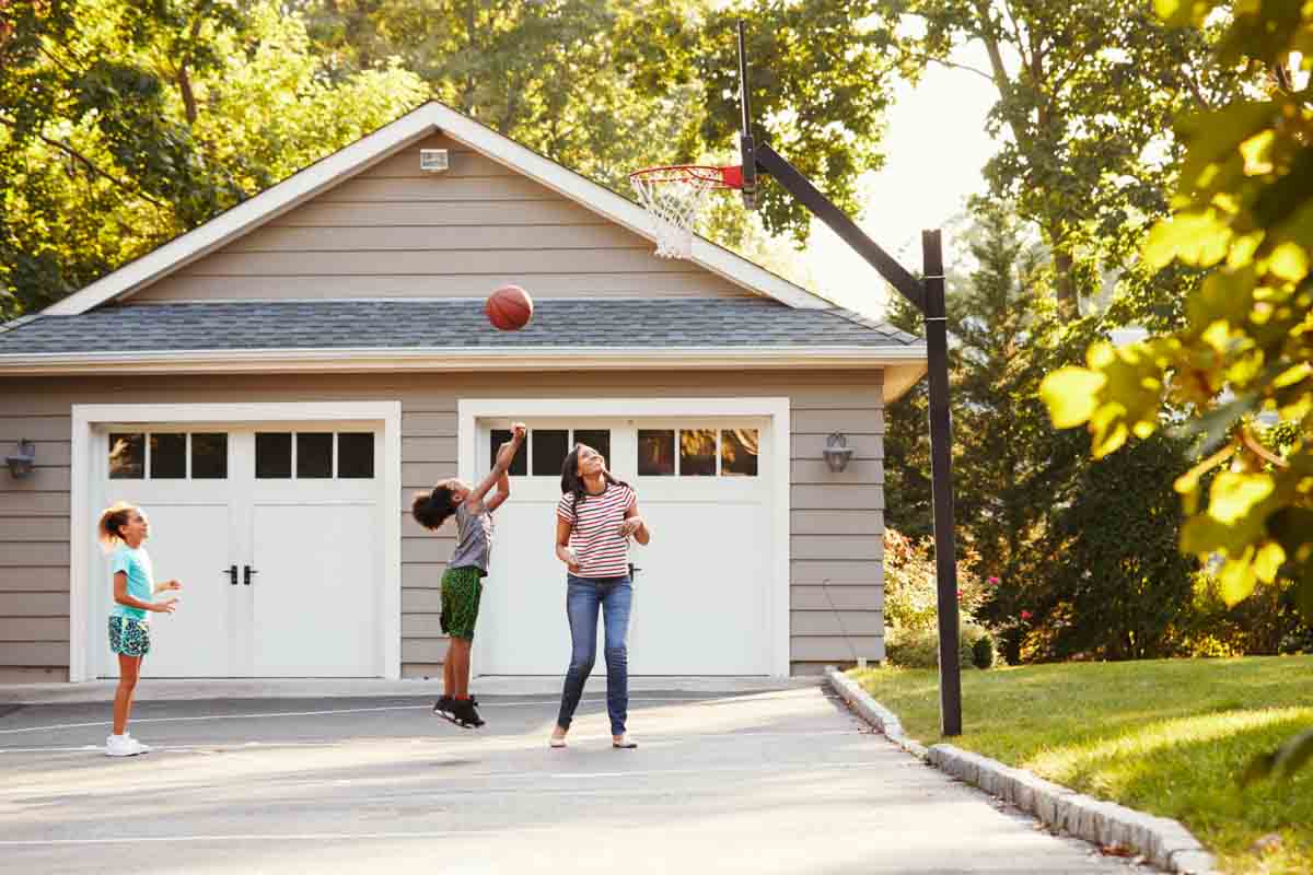 Mother And Children Playing Basketball On Driveway At Home